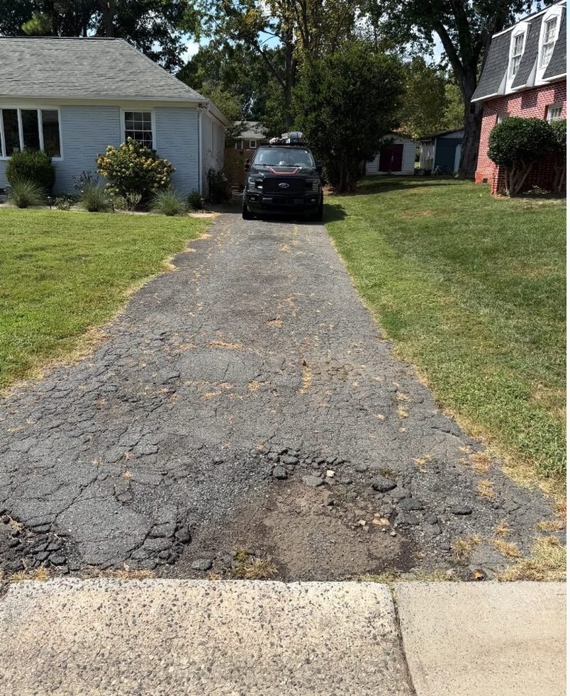 The same driveway before the work, cracked and broken asphalt